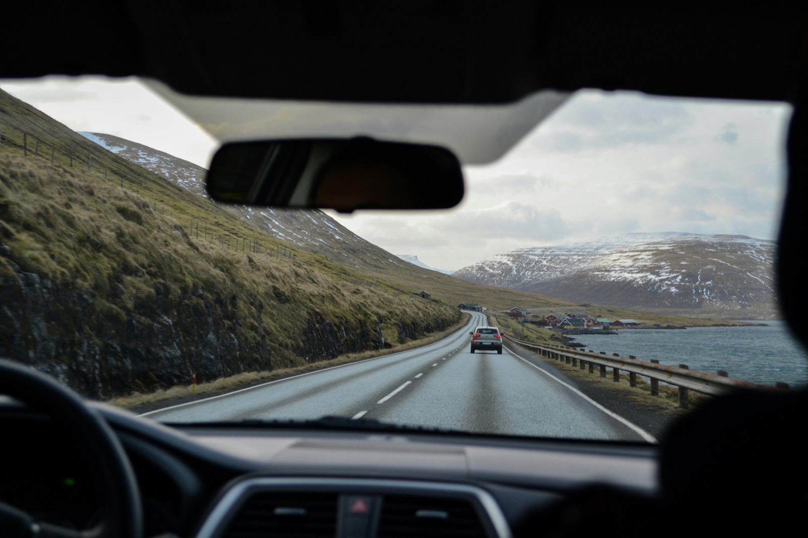 Driving along a Nordic coastal road with mountains and a waterside village