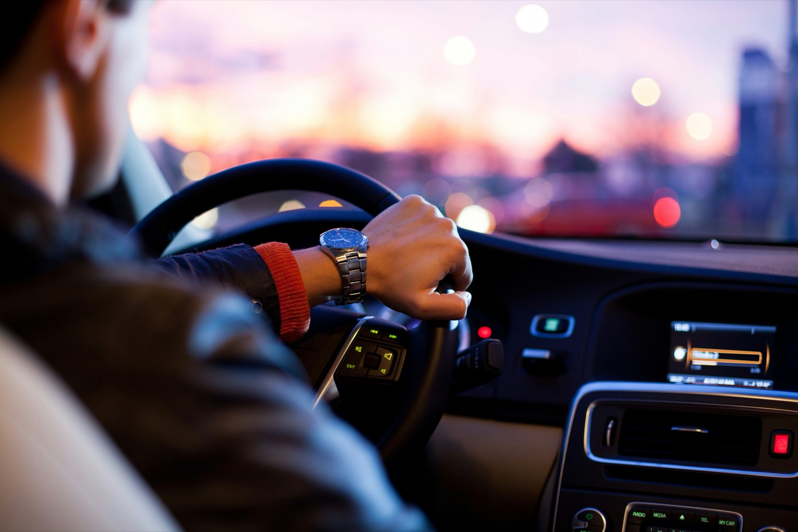 Driver gripping steering wheel at sunset with city lights in background
